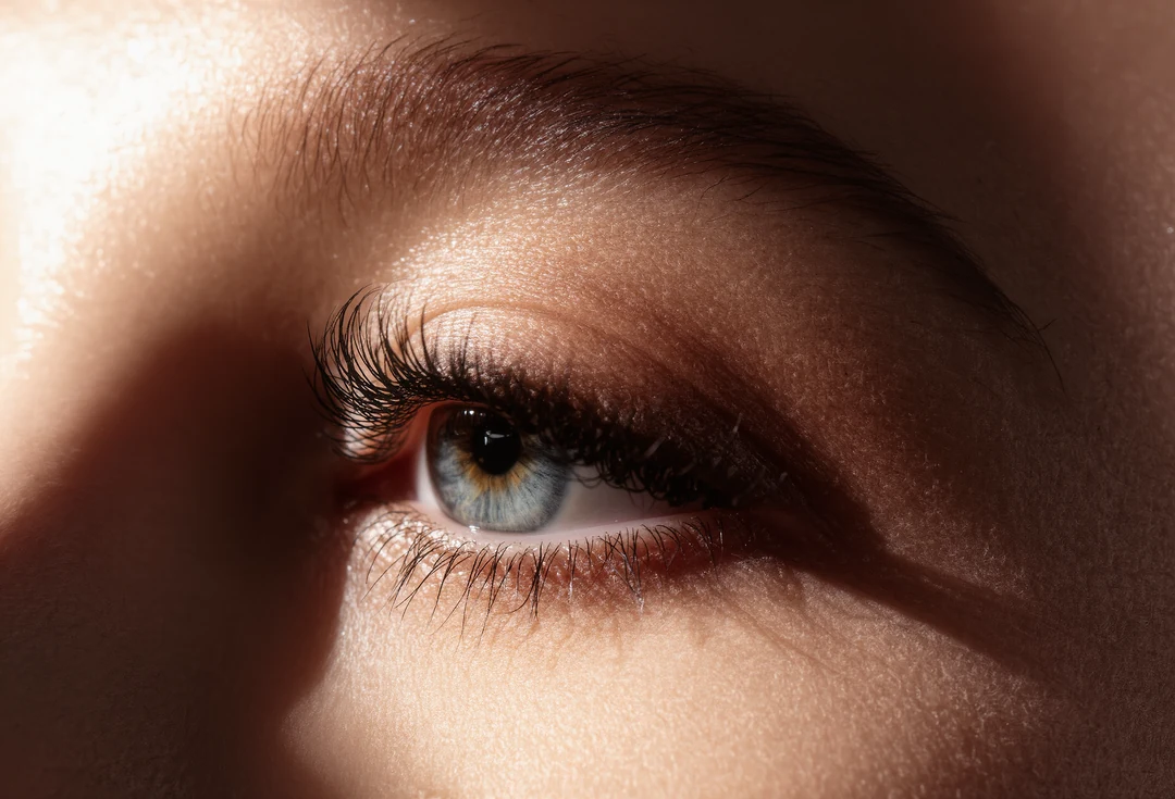 Close-up of a person's face focusing on their eyes and upper nose, showcasing natural skin texture and slight smile lines for a touch of effortless luxury.