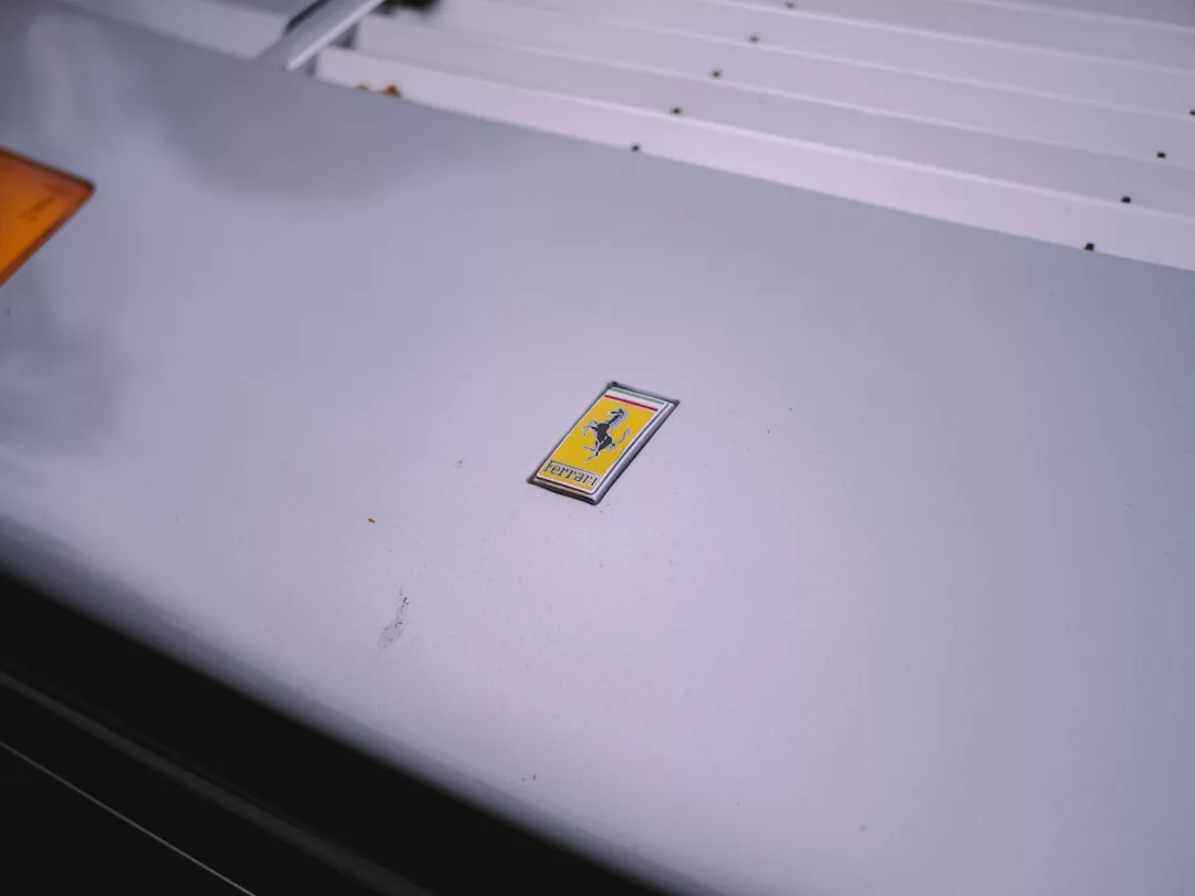 Close-up of a silver car hood featuring a yellow Ferrari logo badge in the center, capturing the Glamesia lifestyle and sense of refined fashion.
