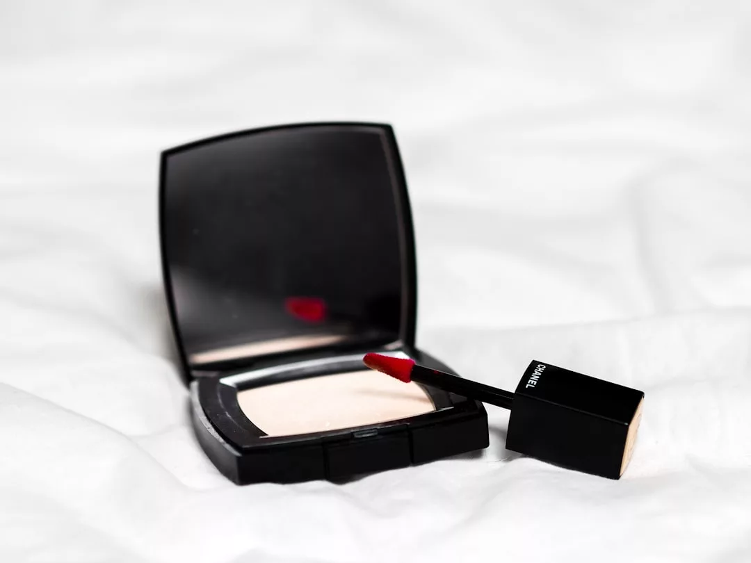 An open compact powder case and a tube of red liquid lipstick with the applicator wand rest on a white fabric surface, capturing Glamesia’s chic fashion and lifestyle essence.