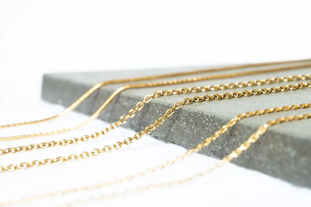 Several luxury gold chains of varying styles are laid out side by side on a gray stone slab against a white background.