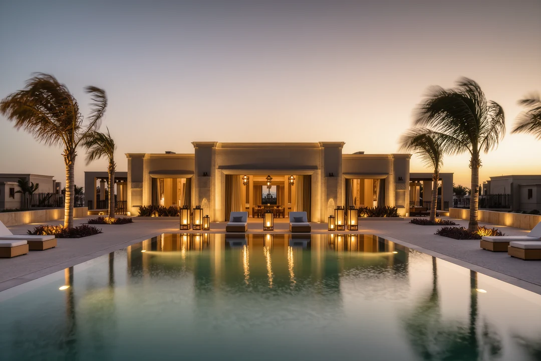 Modern two-story house with large glass windows, wood-paneled ceilings, a balcony, outdoor grill area, and a swimming pool in the foreground under a clear blue sky—perfect for enjoying the Glamesia lifestyle of luxury.