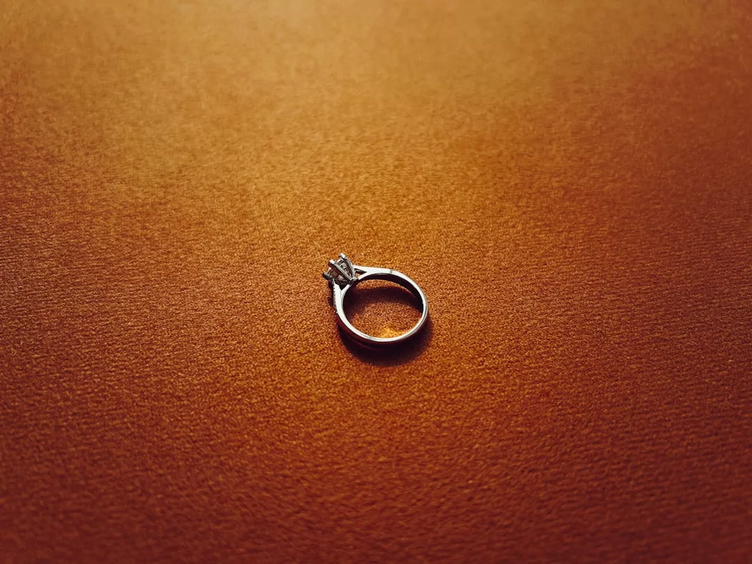 A luxury silver engagement ring with a single diamond is placed on a flat, textured brown surface.